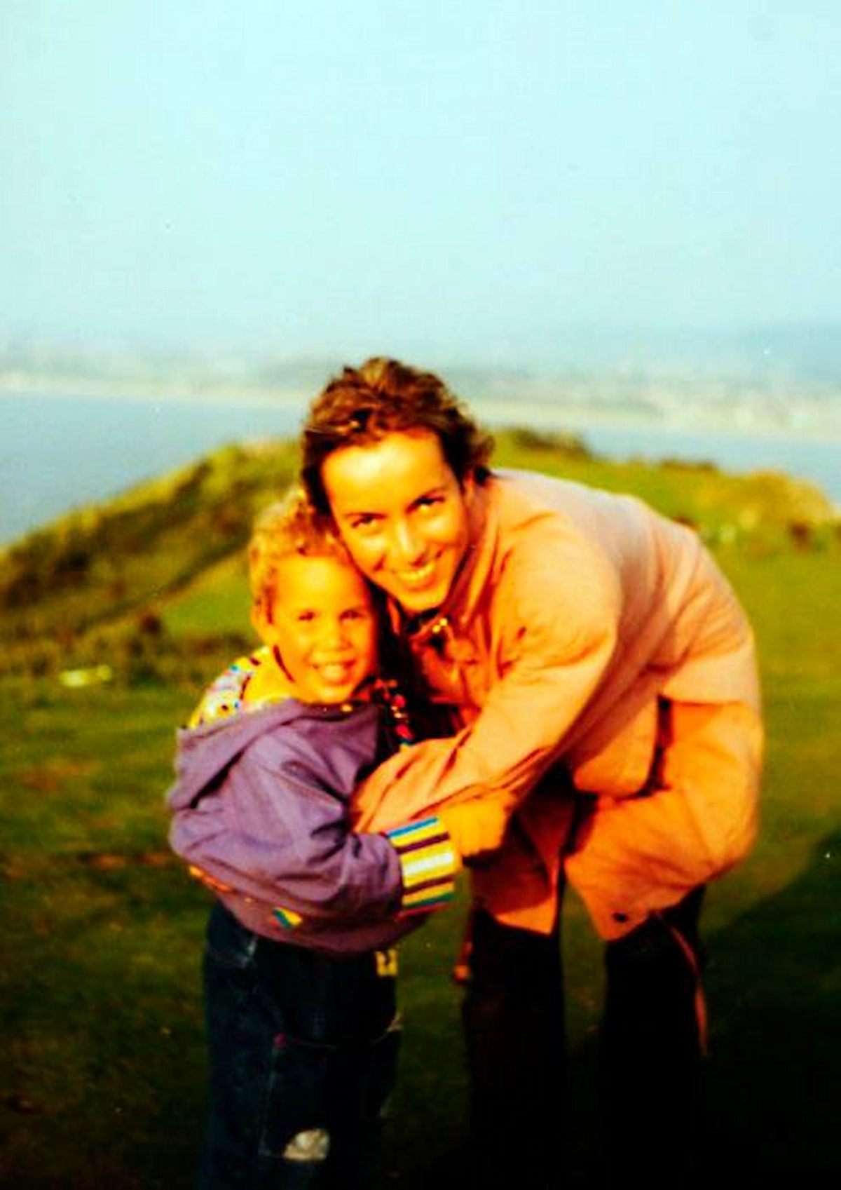 Young Lars smiling with his mother on a green hillside, capturing a joyful childhood moment.