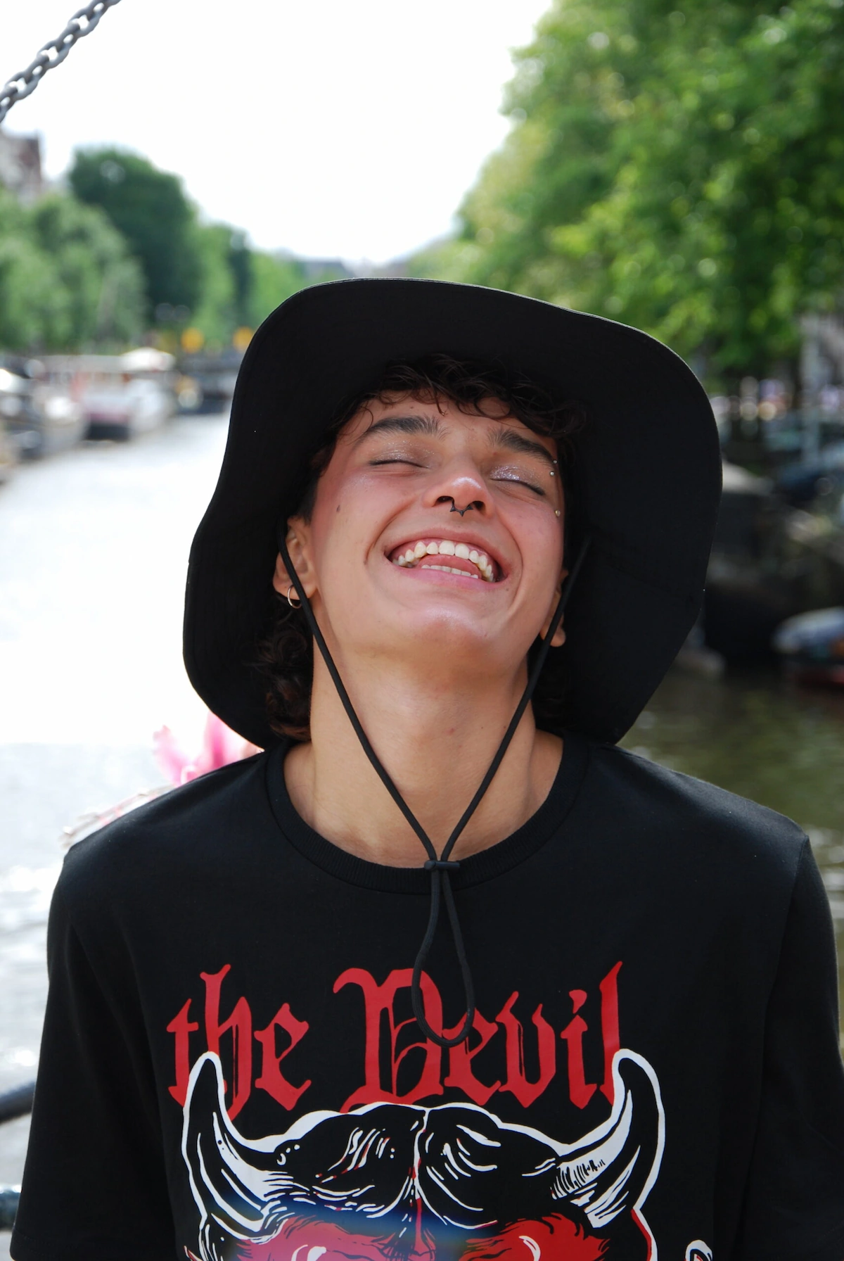 Sebastián Ortiz Colombian model laughing under the sun in Amsterdam, wearing a black hat and enjoying a carefree summer day.