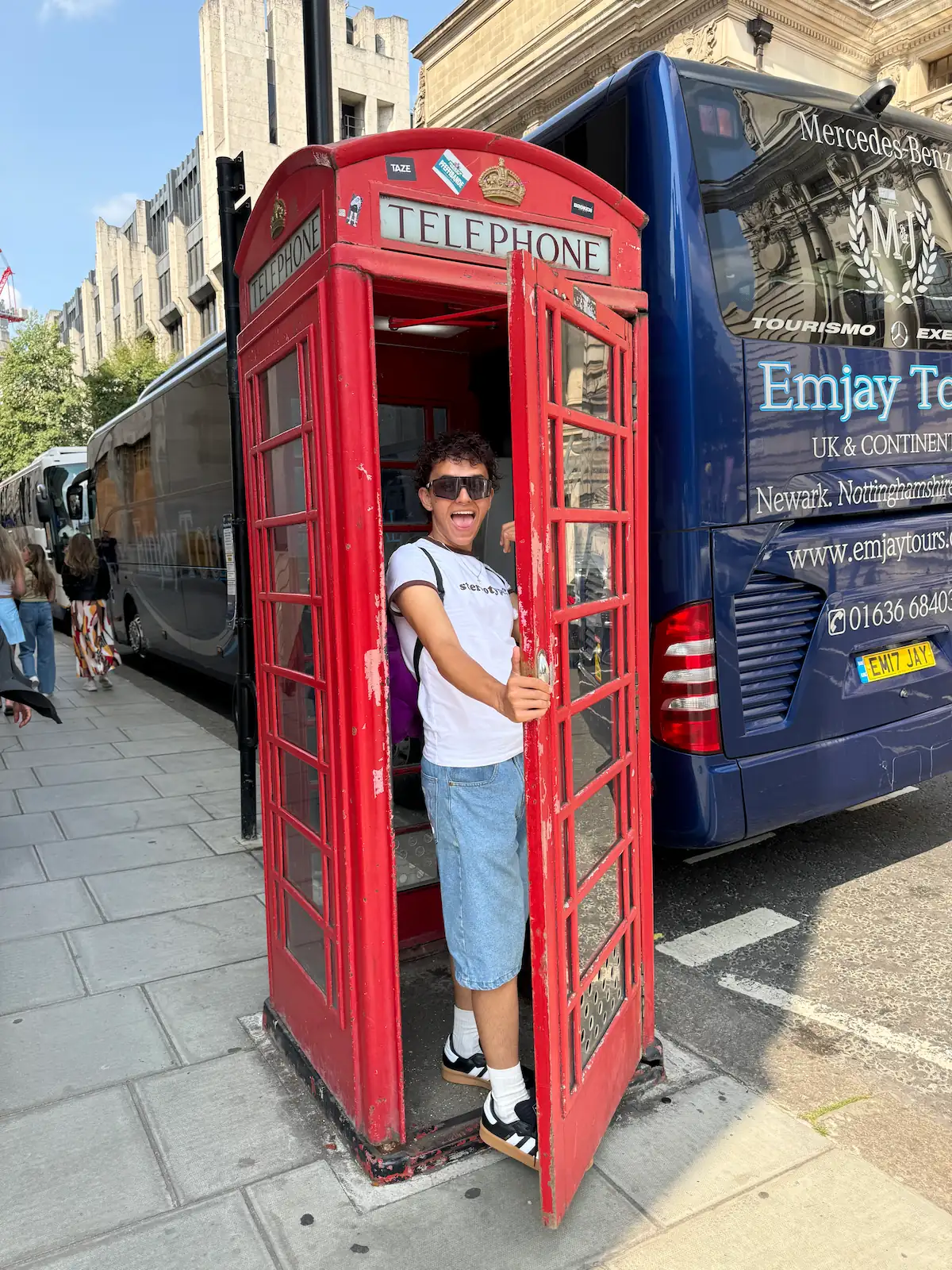 Sebastián Ortiz Colombian model smiling inside a red London phone booth, showing his joyful personality and travel spirit.