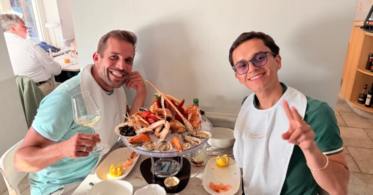 Lars and Sebas enjoying a seafood dinner in Brugge, smiling with fresh oysters, prawns, and wine at their table.