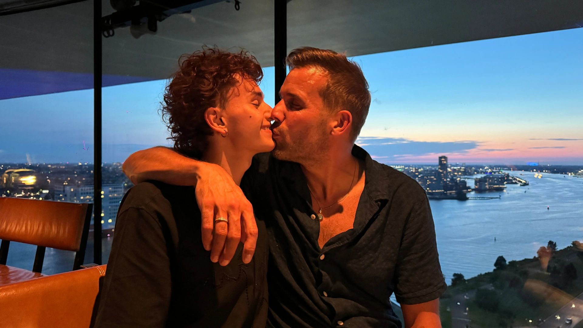 Lars and Sebas from Two Worlds Unite sharing a kiss at sunset overlooking Amsterdam, symbolising love and purpose