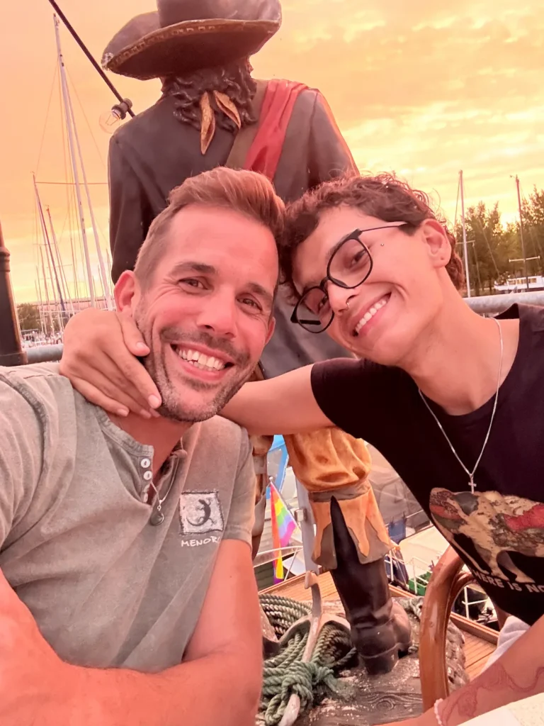 Lars and Sebas smiling together at the harbour during a summer evening, capturing their life by the water.