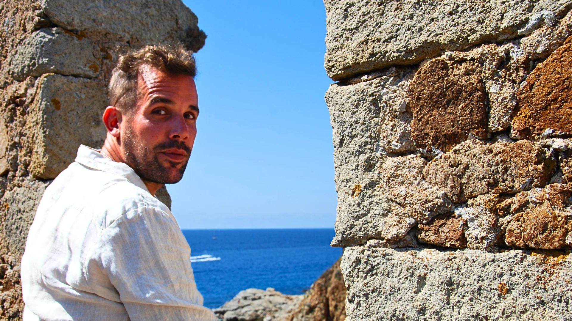 Lars Brunnhoff sitting by a stone wall overlooking the ocean in bright sunlight, reflecting on his guides for building a life you love.