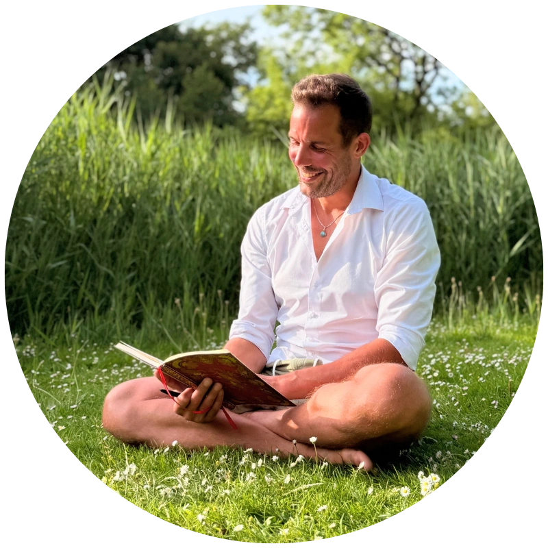 Lars Brunnhoff sitting on the grass in nature, smiling while writing in his journal.